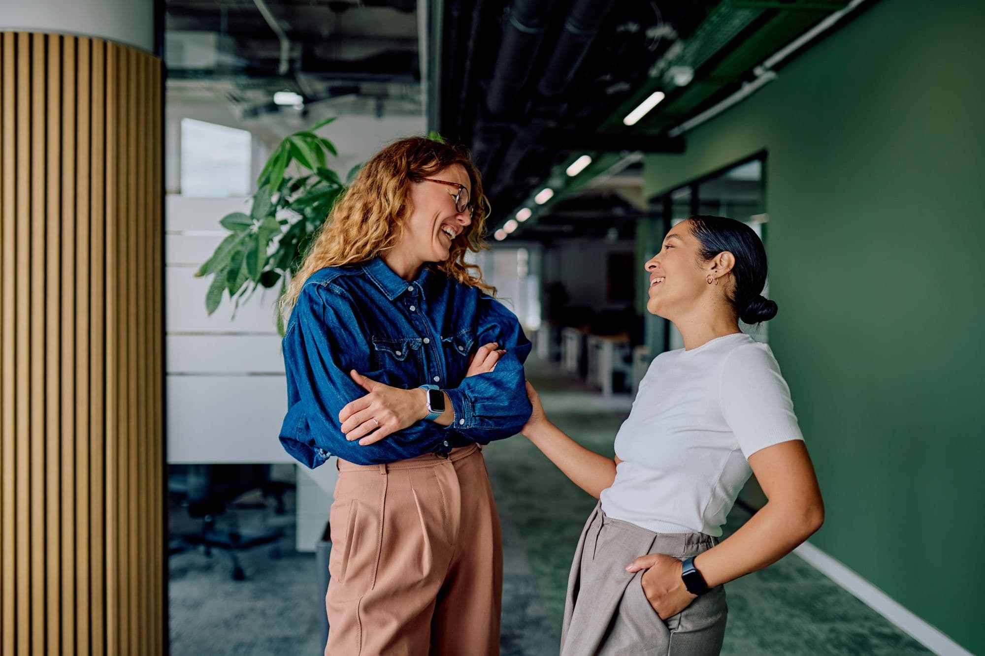 Two colleagues laugh together in an office corridor