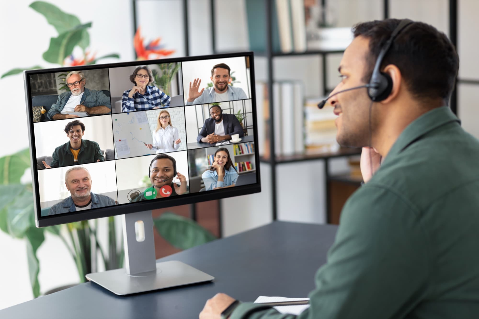 A man with a headset talks with a group of colleagues on a video call