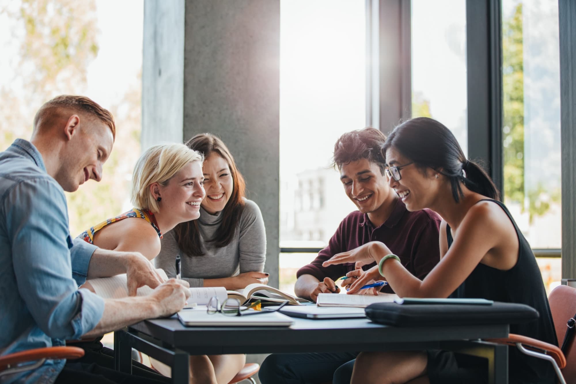 Five colleagues round a table laugh together as one of them explains a point