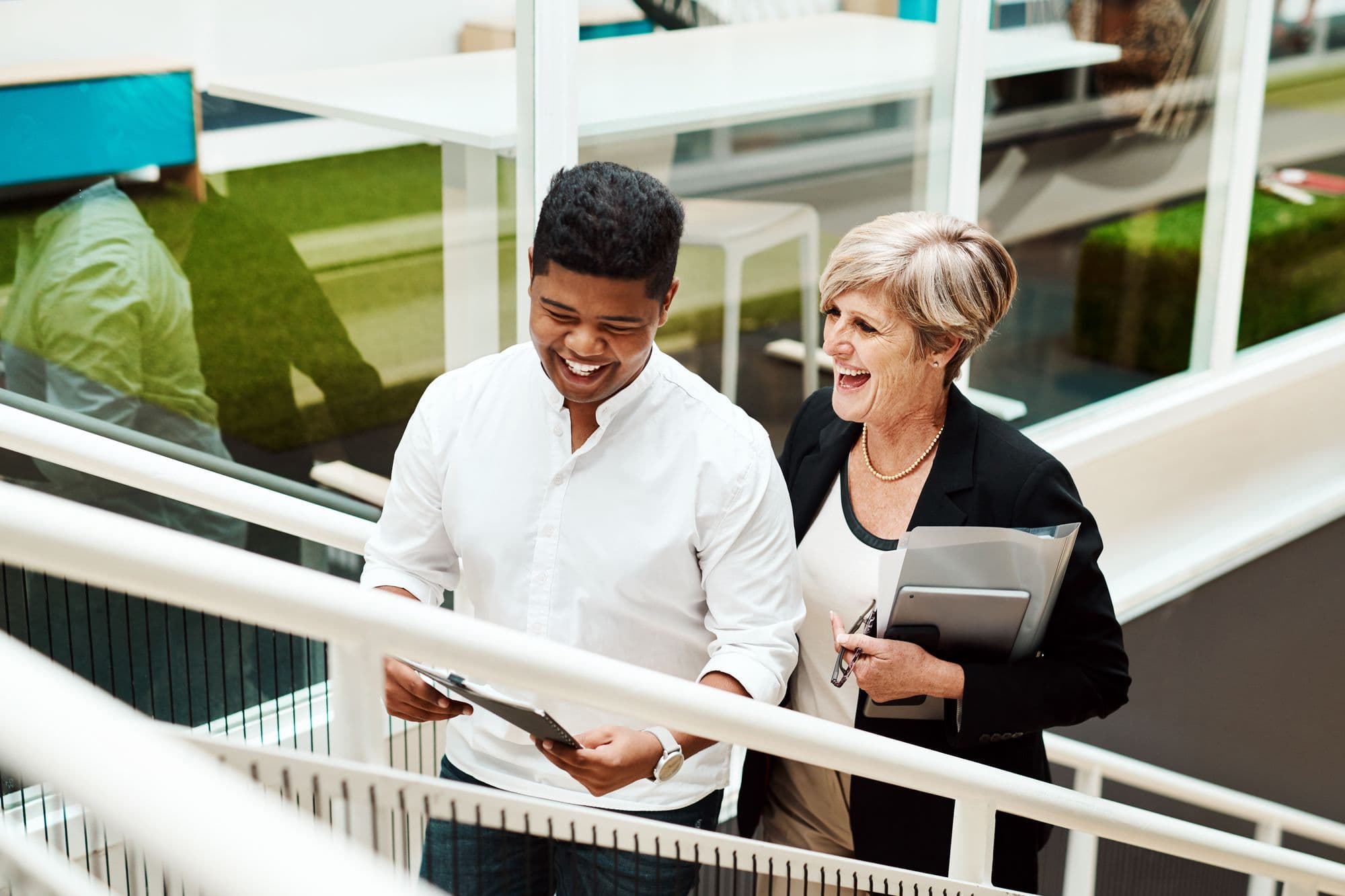 A young man and an older colleague laugh together on the office stairs