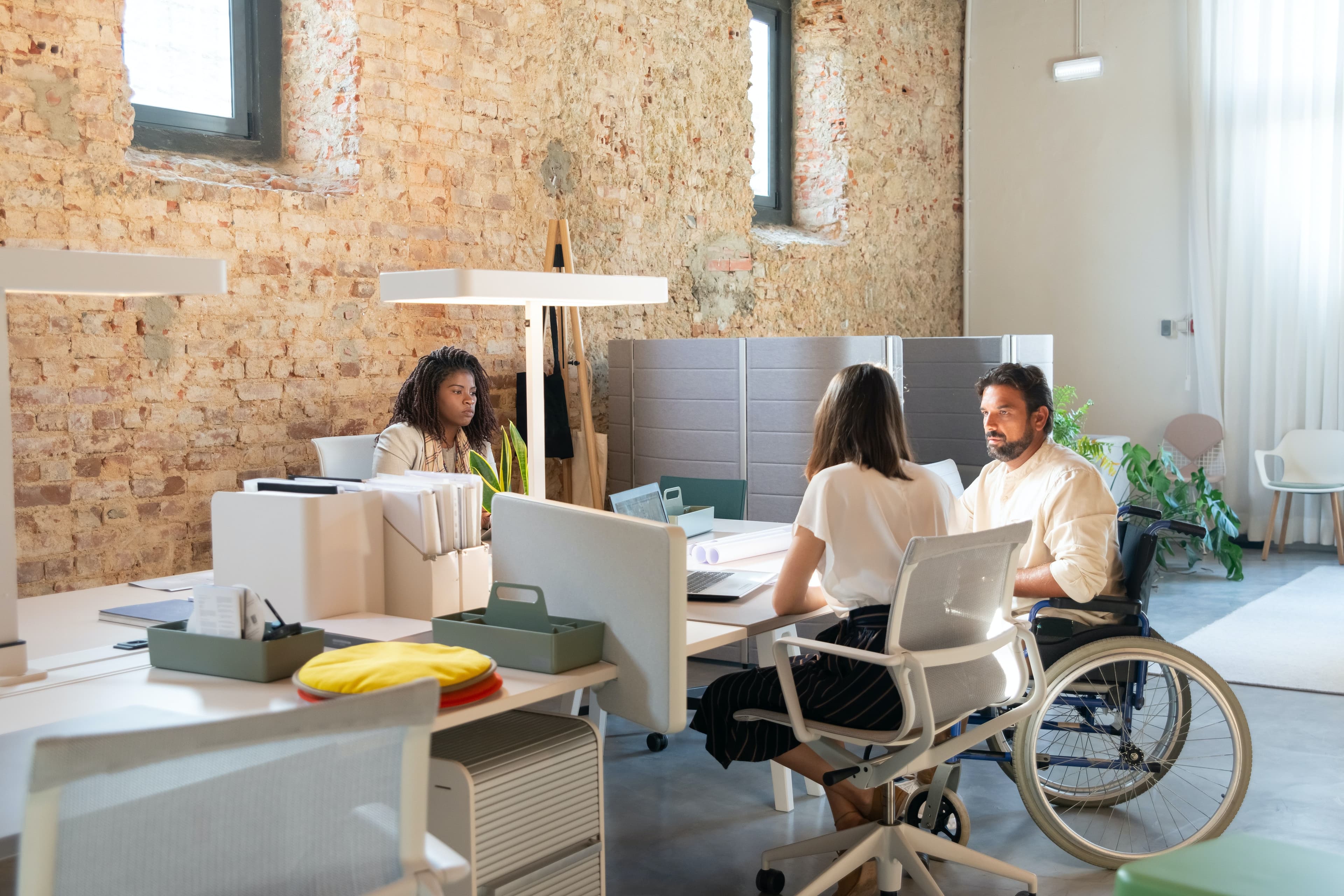 employees practice inclusive behavior at work, female and male colleague sit at table to enable wheelchair access