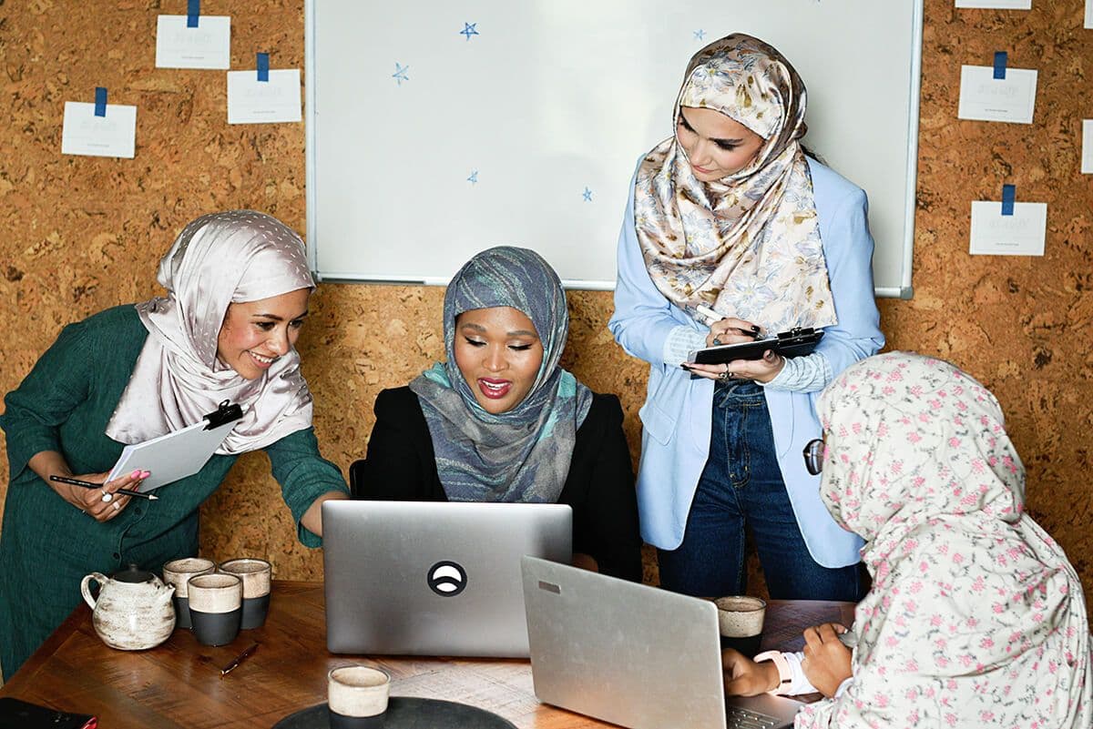 four women in headscarves sitting in an office conference room looking at their laptops. They're planning the new upskilling employees.