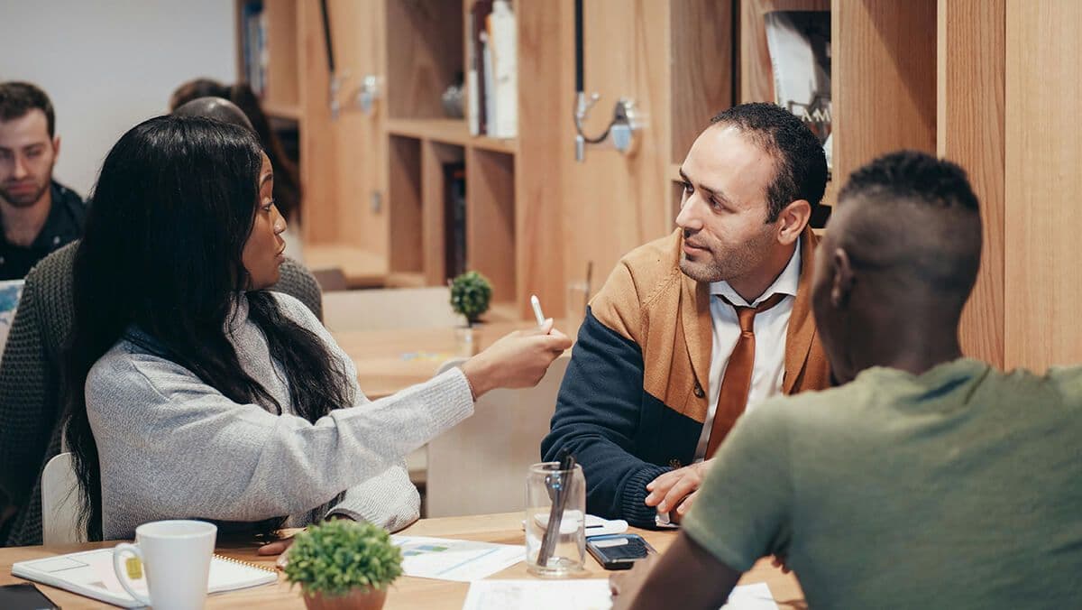 woman employee sitting in an open office space with two male colleagues talking about inclusive workplace cultures.