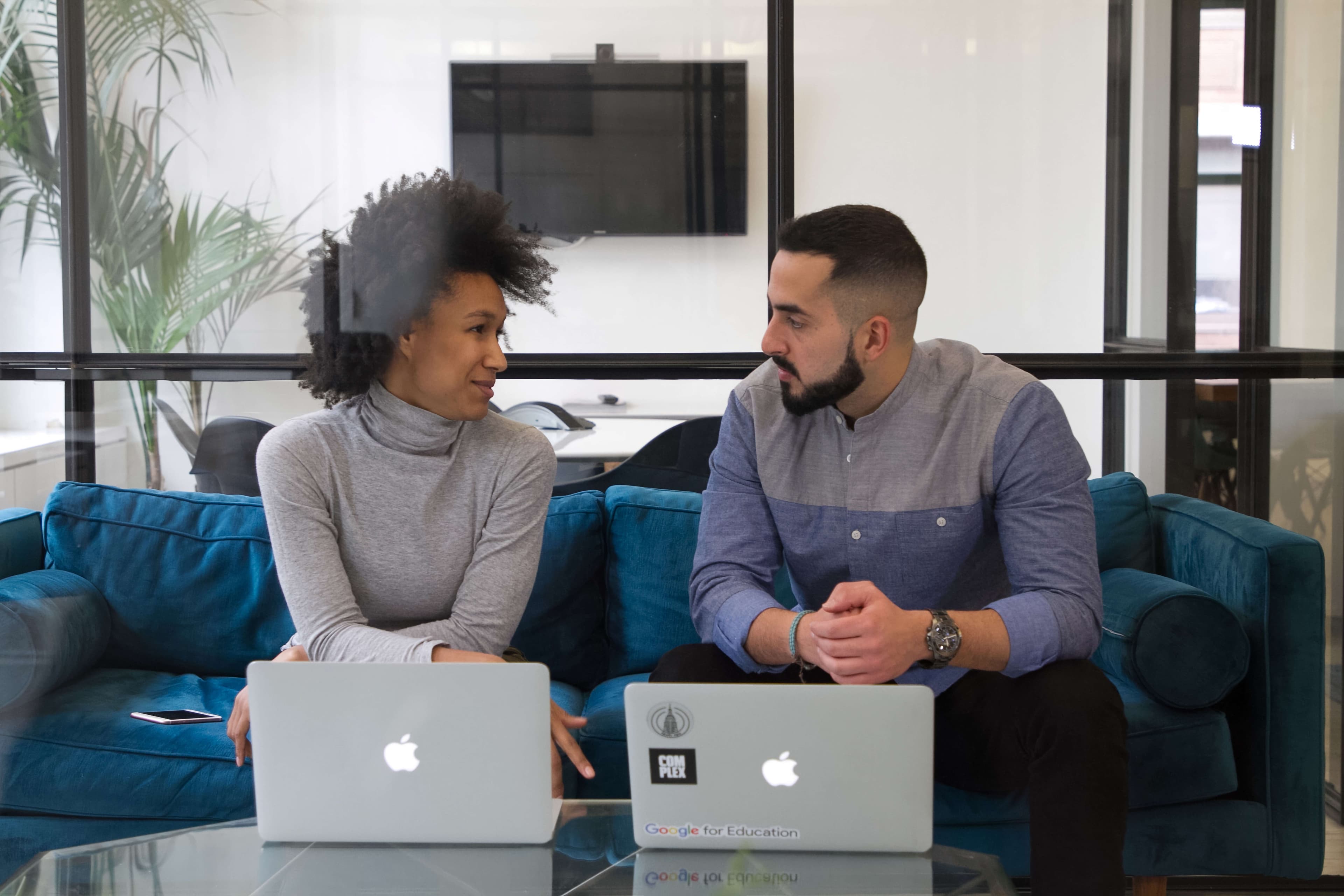 black female employee sits on couch with male employee with laptops open during a reverse mentoring program session