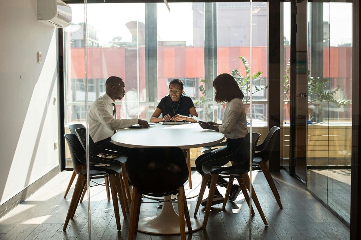 one male colleague and two women sit in a conference room at a table discussing mentorship styles needed for their corporate program