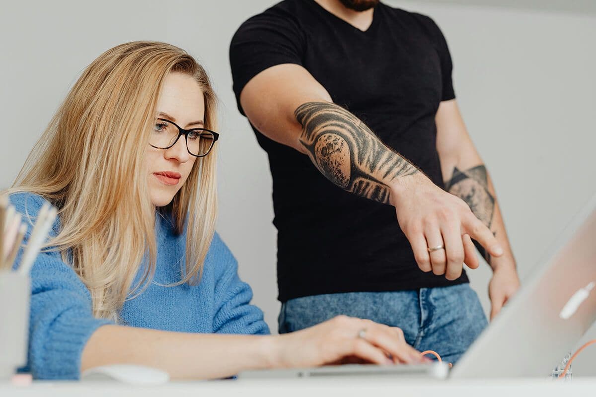 Man pointing at a laptop as a woman works on the computer